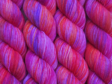 A close up of variegated pinks, crimson, purple and orange coloured skeins of superwash merino and nylon 4ply fingering sock yarn (The Girls Just Wanna Have Fun on Tough Stocking)