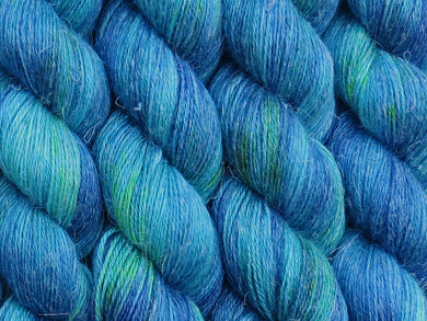 A close up of variegated teal greens and navy blue with speckles of bright yellow coloured skeins of non-superwash baby alpaca, silk and linen 4ply fingering weight yarn (The Other Woman on Spinifex)