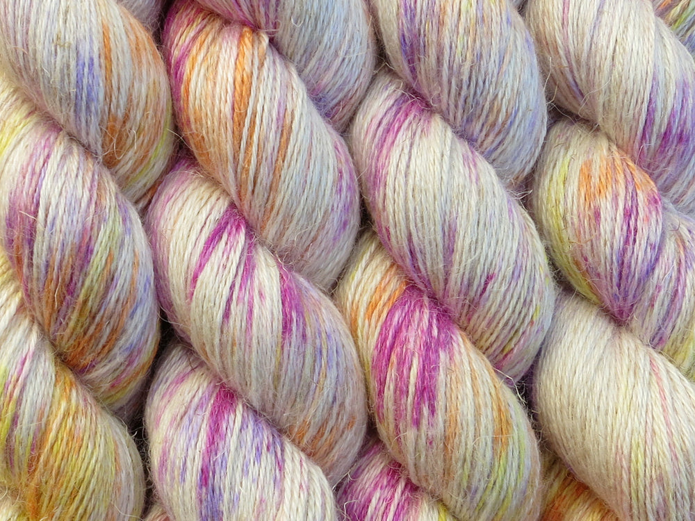 A close up of white with bright speckles of pink, purple, orange and yellow coloured skeins of non-superwash baby alpaca, silk and linen 4ply fingering weight yarn (Titillation on Spinifex)