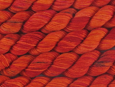 A close up of variegated bright orange, red and fuchsia with black speckles mini skeins of superwash merino and nylon 4ply fingering sock yarn arranged horizontally (Total Fire Ban on Tough Stocking Mini)
