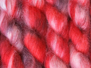 A close up of variegated rich reds with charcoal greys and white coloured skeins of superfine kid mohair and silk 2ply lace yarn (Twelve Collegia on Kid Glove Lace)