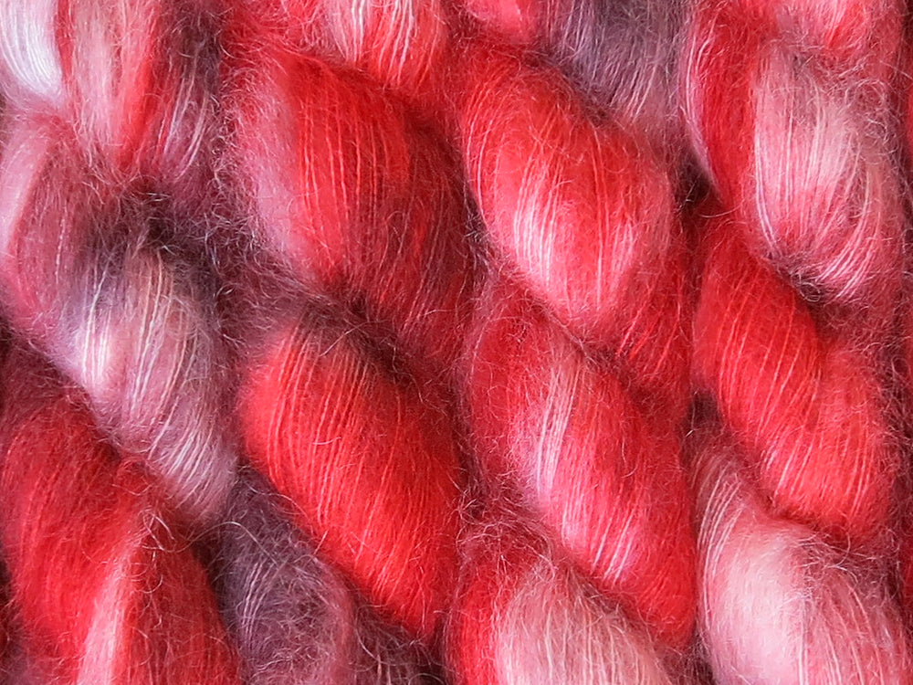 A close up of variegated rich reds with charcoal greys and white coloured skeins of superfine kid mohair and silk 2ply lace yarn (Twelve Collegia on Kid Glove Lace)