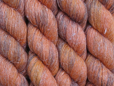 A close up of variegated burnt orange, tangerine and saffron with overtones of caramel and chocolate coloured skeins of non-superwash baby alpaca, silk and linen 4ply fingering weight yarn (Tyger Tyger on Spinifex)