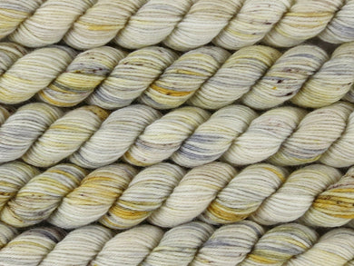 A close up of variegated warm white, golden yellow, grey with brown speckles mini skeins of superwash merino and nylon 4ply fingering sock yarn arranged horizontally (Witchetty Grub on Tough Stocking Mini)