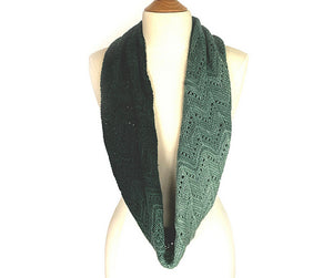 A graduated coloured lace knitted cowl in shades of green hanging on the neck of a cream dress mannequin on a white background. Pattern is Adventurer Cowl by Ambah O'Brien