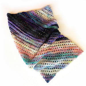 A knitted cowl made from twenty five mini skeins arranged in gradient colour order from purples through greens to creams and pinks through browns to yellows lying on a white background (Adventuring Cowl by Ambah O'Brien)