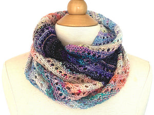 A closeup of a knitted cowl made from twenty five mini skeins arranged in gradient colour order from purples through greens to creams and pinks through browns to yellows arranged cozily around the neck of a cream dress mannequin on a white background (Adventuring Cowl by Ambah O'Brien)