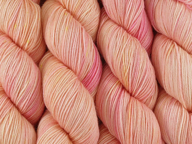A close up of semi-solid warm soft apricot with hints of golden yellow and red pink coloured skeins of superwash merino and nylon 4ply fingering sock yarn (Apricot Nectar on Tough Stocking)