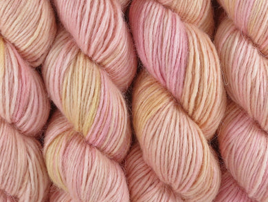 A close up of semi-solid warm soft apricot with hints of golden yellow and red pink coloured skeins of alpaca merino and silk singles DK 8ply yarn (Apricot Nectar on Nuzzle)