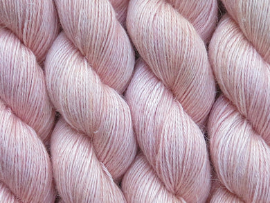 A close up of semi-solid warm soft apricot with hints of golden yellow and red pink coloured skeins of non-superwash baby alpaca, silk and linen 4ply fingering weight yarn (Apricot Nectar on Spinifex)