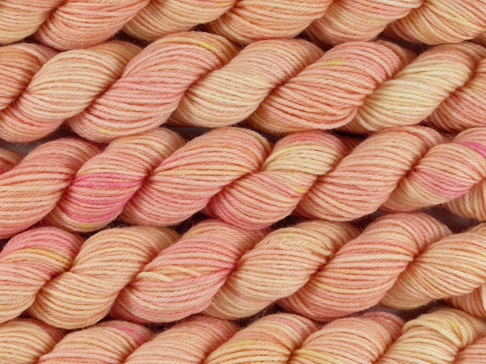 A close up of semi-solid warm soft apricot with hints of golden yellow and red pink mini skeins of superwash merino and nylon 4ply fingering sock yarn arranged horizontally (Apricot Nectar on Tough Stocking Mini)