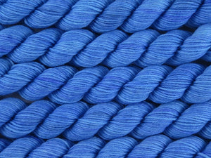 A close up of bright semi-solid medium to light blue with hints of darker blue-violet mini skeins of superwash merino and nylon 4ply fingering sock yarn arranged horizontally (Autumn Sky on Tough Stocking Mini)