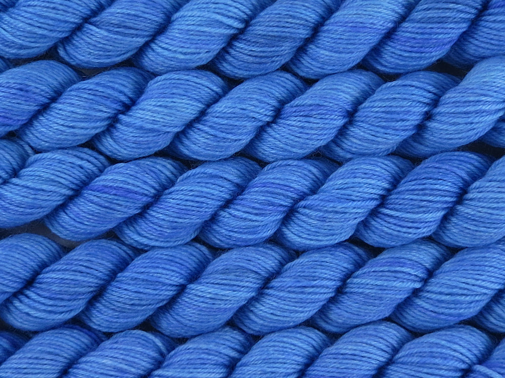 A close up of bright semi-solid medium to light blue with hints of darker blue-violet mini skeins of superwash merino and nylon 4ply fingering sock yarn arranged horizontally (Autumn Sky on Tough Stocking Mini)