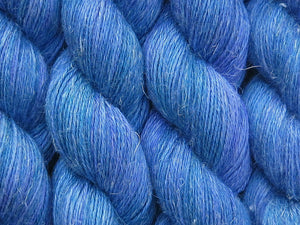 A close up of variegated medium blue with hints of teal green and blue-violet coloured skeins of non-superwash baby alpaca, silk and linen 4ply fingering weight yarn (Bass Strait on Spinifex)