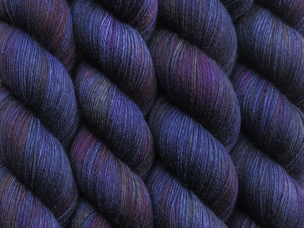 A close up of variegated black with hints of yellow, orange, pink and purple coloured skeins of superwash merino and nylon 4ply fingering sock yarn (Big Bazookas on Tough Stocking)