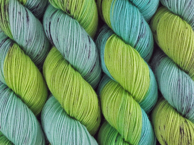A close up of variegated bright light lime and mint greens with black speckles coloured skeins of superwash merino and nylon 4ply fingering sock yarn (Black Kangaroo Paw on Tough Stocking)