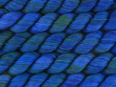 A close up of variegated bright blue, deep violet and emerald green mini skeins of superwash merino and nylon 4ply fingering sock yarn arranged horizontally (Blue Quandong on Tough Stocking Mini)