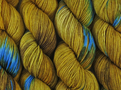 A close up of variegated yellow and brown with flashes of brilliant aqua blue coloured skeins of superwash merino and nylon 4ply fingering sock yarn (Blue Ring Octopus on Tough Stocking)