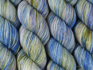 A close up of variegated cobalt blue, white, moss green and violet coloured skeins of superwash bluefaced leicester, silk and cashmere 4ply fingering sock yarn (Blue Swimmer Crab on Blue Chip Stocking)