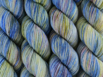 A close up of variegated cobalt blue, white, moss green and violet coloured skeins of superwash merino and nylon 4ply fingering sock yarn (Blue Swimmer Crab on Tough Stocking)