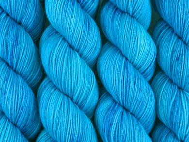 A close up of semi-solid bright blue with speckles of deep blue coloured skeins of superwash merino and nylon 4ply fingering sock yarn (Boogie Blues on Tough Stocking)
