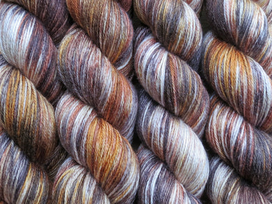 A close up of variegated ebony, chocolate, chestnut and beige brown coloured skeins of superwash merino and silk 4ply fingering sock yarn (Bungil on Silk Stocking)