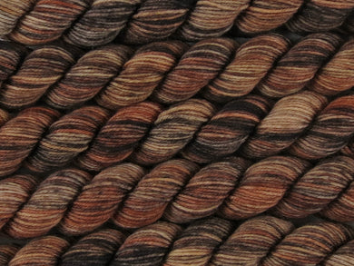 A close up of multiple variegated ebony, chocolate, chestnut and beige brown mini skeins of superwash merino and nylon 4ply fingering sock yarn arranged horizontally (Bungil on Tough Stocking Mini)