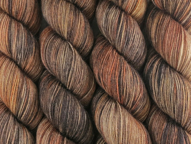 A close up of variegated ebony, chocolate, chestnut and beige brown coloured skeins of superwash merino and nylon 4ply fingering sock yarn (Bungil on Tough Stocking)