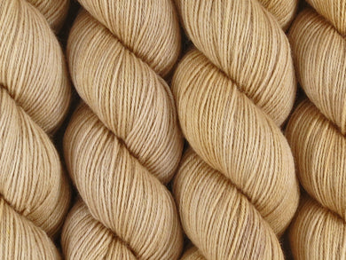 A close up of semi-solid light warm beige tan coloured skeins of superwash merino and nylon 4ply fingering sock yarn (Buttergin on Tough Stocking)