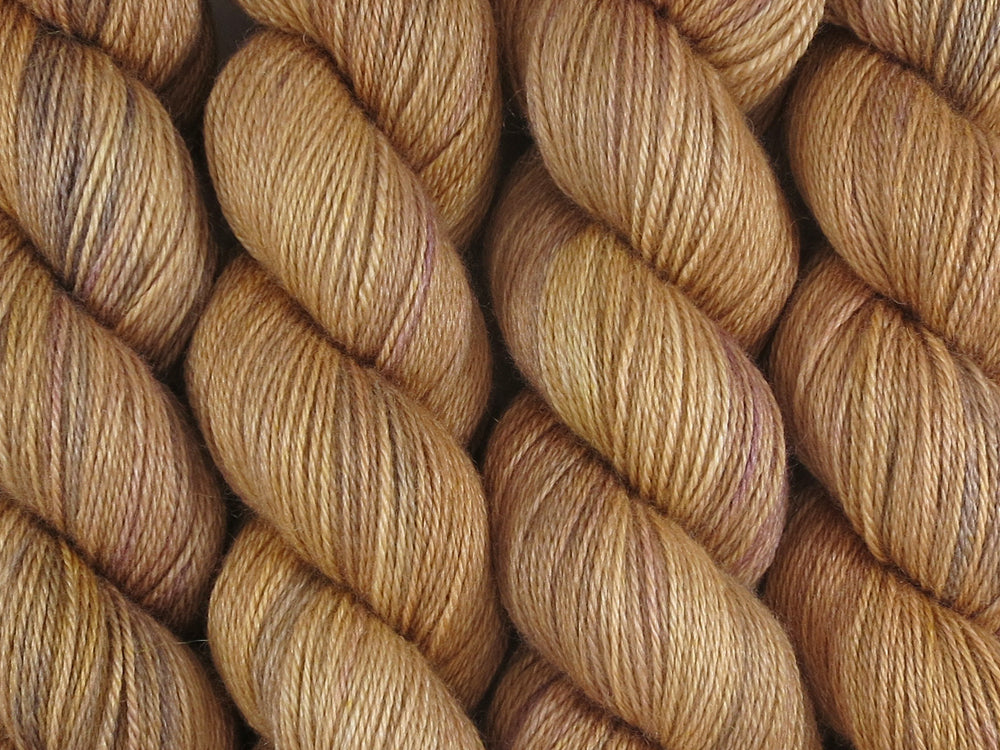 A close up of semi-solid warm tan with hints of orange, dark cocoa and maroon coloured skeins of superwash bluefaced leicester, silk and cashmere 4ply fingering sock yarn (Butterscotch on Blue Chip Stocking)