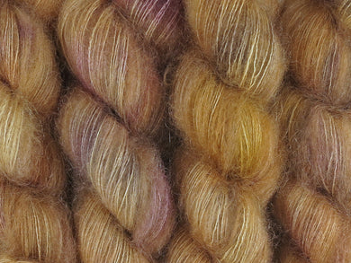 A close up of semi-solid warm tan with hints of orange, dark cocoa and maroon coloured skeins of superfine kid mohair and silk 2ply lace yarn (Butterscotch on Kid Glove Lace)