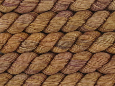 A close up of semi-solid warm tan with hints of orange, dark cocoa and maroon mini skeins of superwash merino and nylon 4ply fingering sock yarn arranged horizontally (Butterscotch on Tough Stocking Mini)
