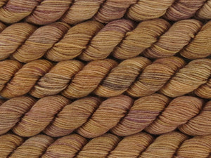 A close up of semi-solid warm tan with hints of orange, dark cocoa and maroon mini skeins of superwash merino and nylon 4ply fingering sock yarn arranged horizontally (Butterscotch on Tough Stocking Mini)
