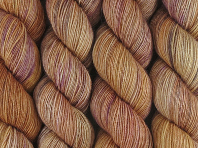 A close up of semi-solid warm tan with hints of orange, dark cocoa and maroon coloured skeins of superwash merino and nylon 4ply fingering sock yarn (Butterscotch on Tough Stocking)