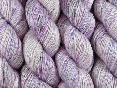 A close up of variegated white yarn with speckled hints of black fuchsia and purple coloured skeins of superwash merino and silk 4ply fingering sock yarn (Candy Is Dandy on Silk Stocking)