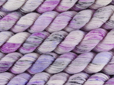 A close up of variegated white yarn with speckled hints of black fuchsia and purple mini skeins of superwash merino and nylon 4ply fingering sock yarn arranged horizontally (Candy Is Dandy on Tough Stocking Mini)