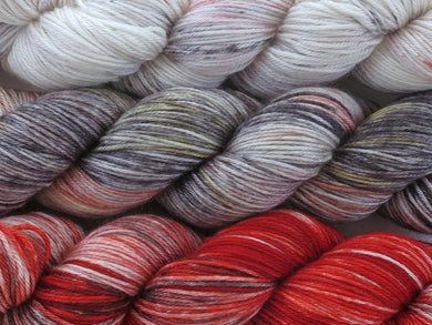 A close up of three variegated skeins of yarn from white with red and black speckles at the top to grey, black, yellow, rust red and white in the middle to reds, black and white at the bottom (Eiffel Tower Cityscape Impressionists MKAL Yarn Kit on Silk Stocking)