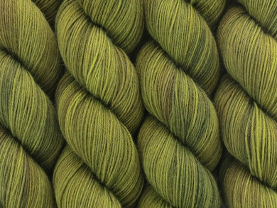 A close up of semi-solid mid-khaki green with hints of brown, chartreuse and golden tan coloured skeins of superwash merino and nylon 4ply fingering sock yarn (Fatigued on Tough Stocking)