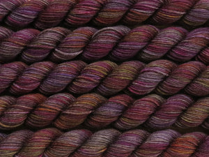 A close up of variegated charcoal grey with hints of yellow, orange, pink and purple mini skeins of superwash merino and nylon 4ply fingering sock yarn arranged horizontally (Filthy Pillows on Tough Stocking Mini)