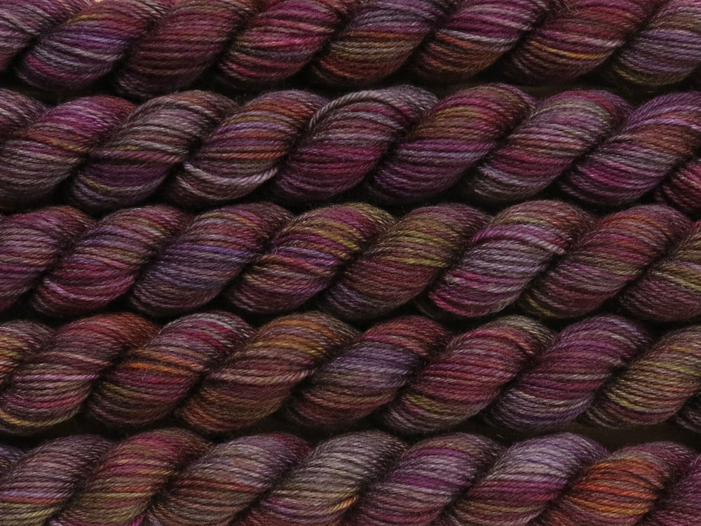 A close up of variegated charcoal grey with hints of yellow, orange, pink and purple mini skeins of superwash merino and nylon 4ply fingering sock yarn arranged horizontally (Filthy Pillows on Tough Stocking Mini)