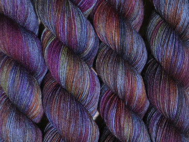 A close up of variegated charcoal grey with hints of yellow, orange, pink and purple coloured skeins of superwash merino and nylon 4ply fingering sock yarn (Filthy Pillows on Tough Stocking)