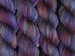 A close up of variegated charcoal grey with hints of yellow, orange, pink and purple coloured skeins of superwash merino and nylon 4ply fingering sock yarn (Filthy Pillows on Tough Stocking)