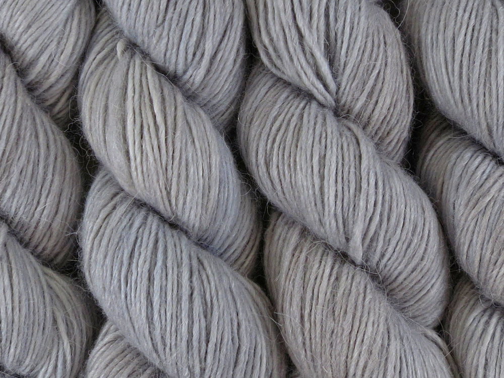 A close up of semi-solid grey with hints of silver, graphite and steel blue coloured skeins of alpaca merino and silk singles DK 8ply yarn (Fog Bound on Nuzzle)