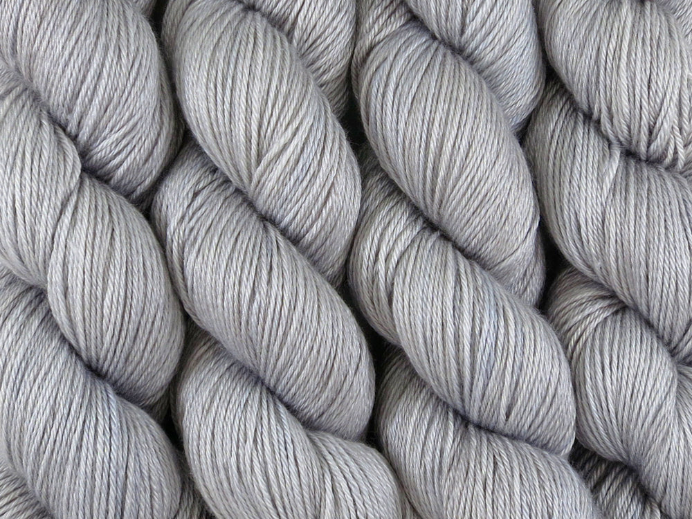 A close up of semi-solid grey with hints of silver, graphite and steel blue coloured skeins of superwash merino and silk 4ply fingering sock yarn (Fog Bound on Silk Stocking)