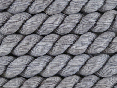A close up of semi-solid grey with hints of silver, graphite and steel blue mini skeins of superwash merino and nylon 4ply fingering sock yarn arranged horizontally (Fog Bound on Tough Stocking Mini)