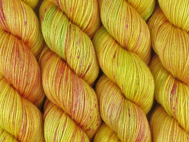 A close up of variegated bright yellows with hints of lime green and speckles of red and pink coloured skeins of superwash merino and silk 4ply fingering sock yarn (Freckled Sun Orchid on Silk Stocking)