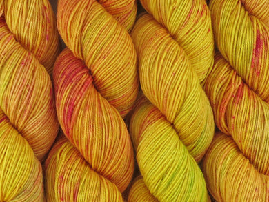 A close up of variegated bright yellow and lime green with speckles of red and pink coloured skeins of superwash merino and nylon 4ply fingering sock yarn (Freckled Sun Orchid on Tough Stocking)