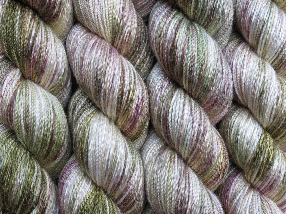 A close up of variegated khaki and forest greens, ecru and brown coloured skeins of superwash merino and silk 4ply fingering sock yarn (Gone Bush on Silk Stocking)