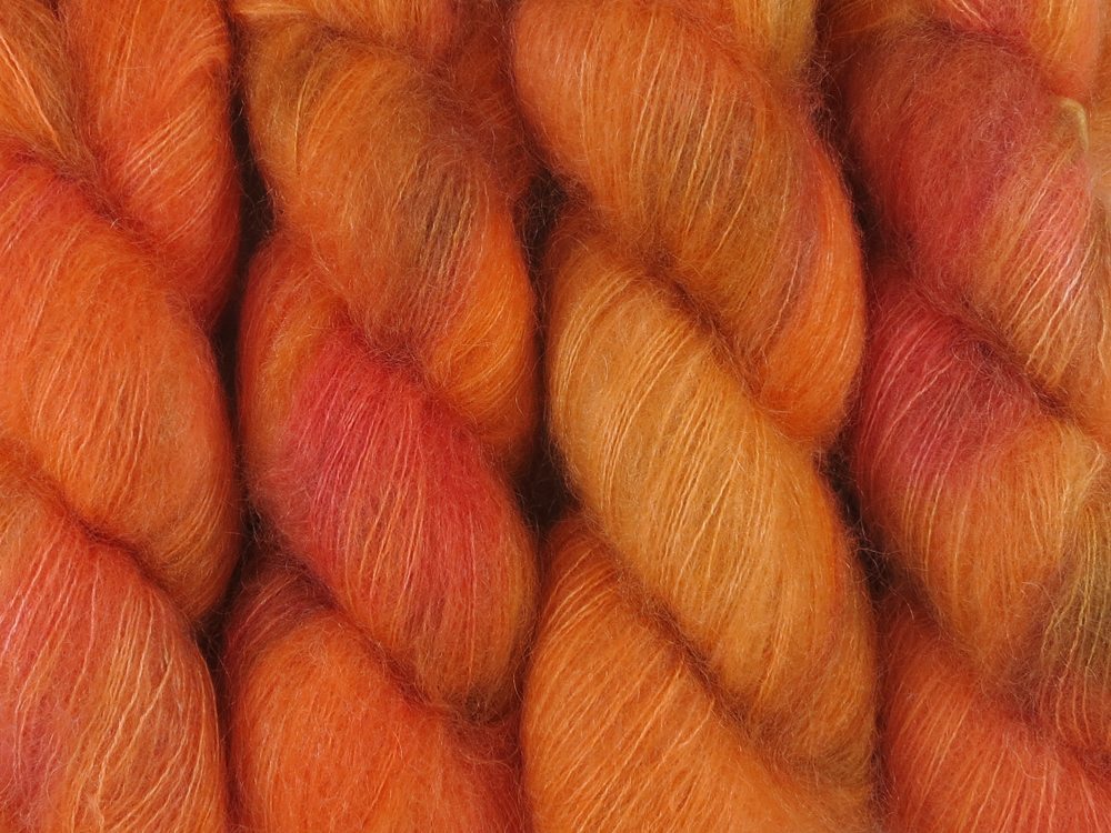 A close up of variegated bright orange, coral, hot pink and moss green coloured skeins of superfine kid mohair and silk 2ply lace yarn (Gorgon's Head Coral on Kid Glove Lace)