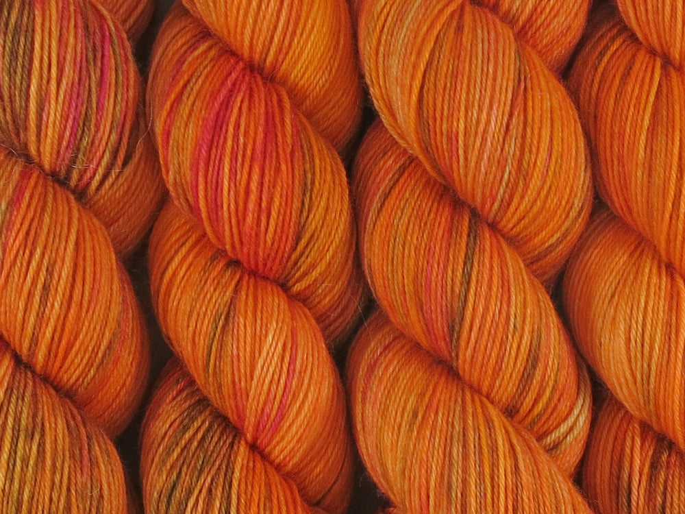 A close up of variegated bright orange, coral, hot pink and moss green coloured skeins of superwash merino and nylon 4ply fingering sock yarn (Gorgon's Head Coral on Tough Stocking)
